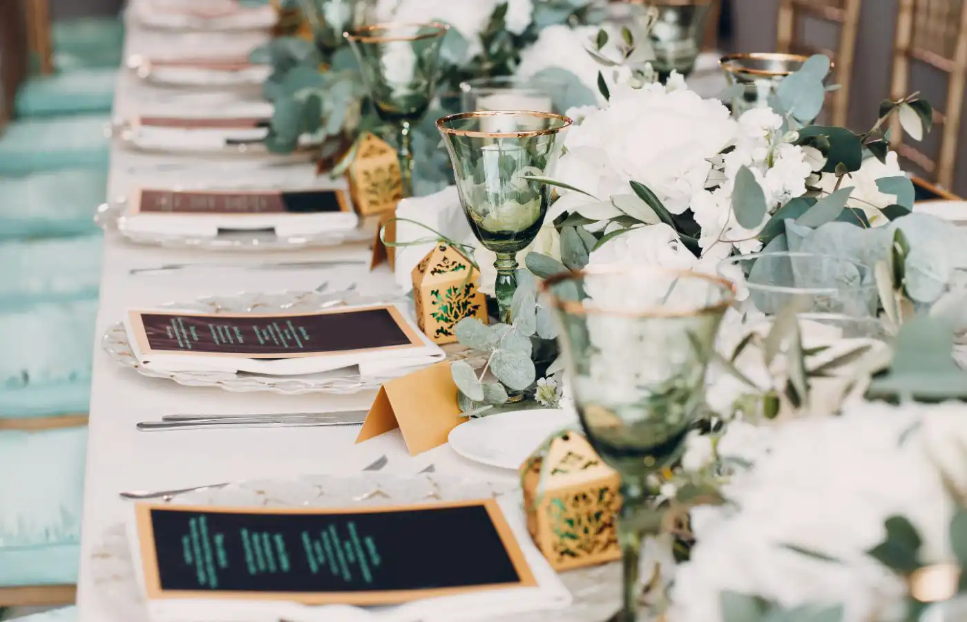 Table élégamment dressée avec verrerie dorée, menus personnalisés et décoration florale pour un événement haut de gamme.