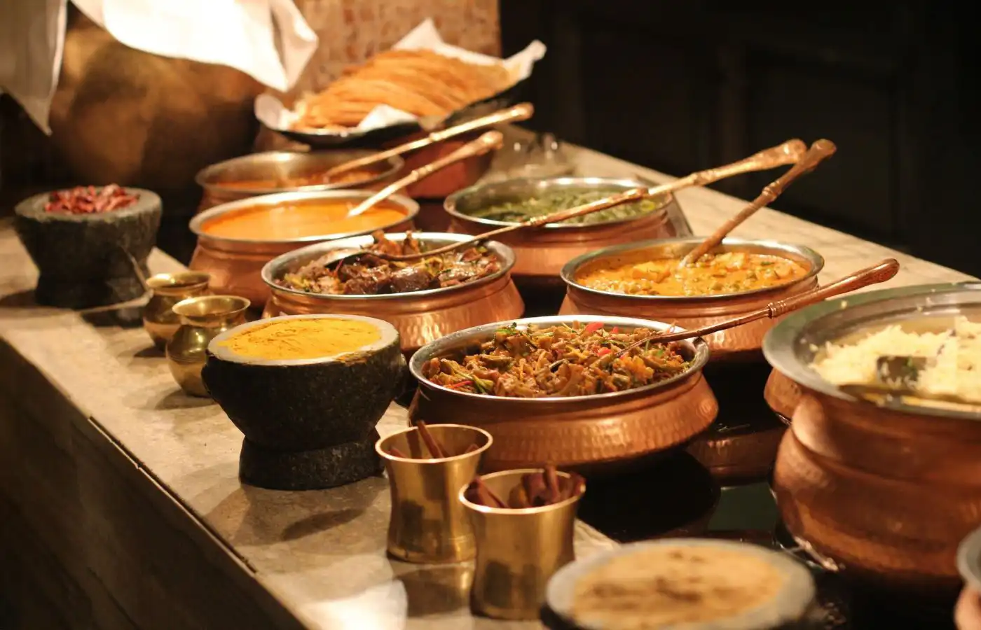 Buffet à thème avec des plats exotiques dans des marmites en cuivre, illustrant un voyage culinaire inspiré de la cuisine indienne.